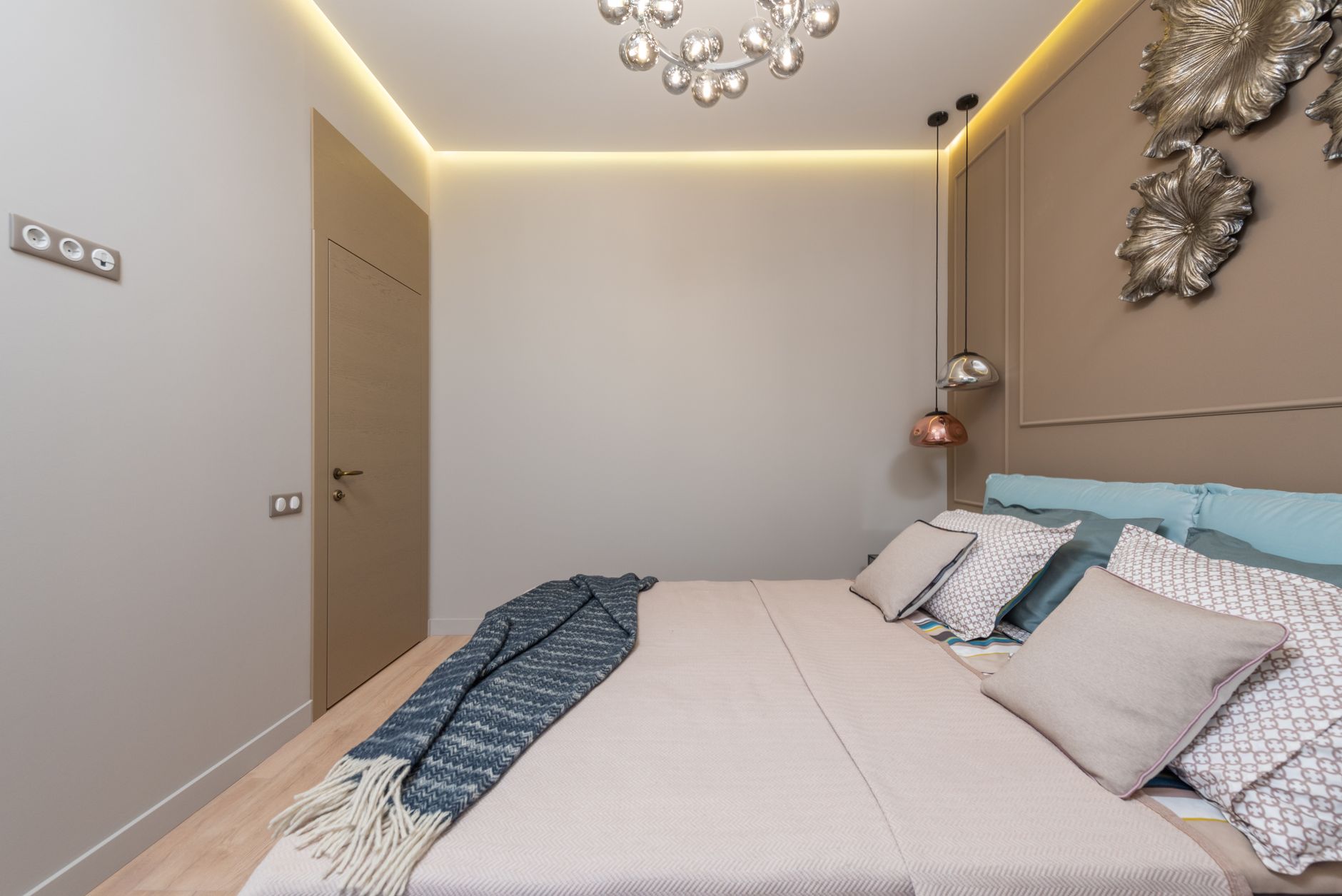 Interior of hotel room with bed with pillows and blanket next to lamps hanging from ceiling near door