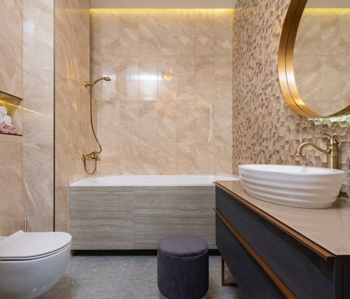 Contemporary bathroom with toilet bowl against washbasin on cabinet under mirror reflecting tiled wall in hotel