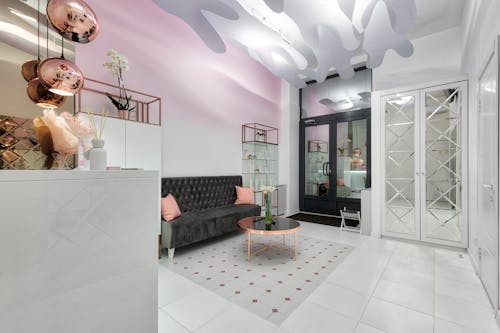 Contemporary lobby interior with sofa and table against doors illuminated by shiny lamps above tiled floor with ornament