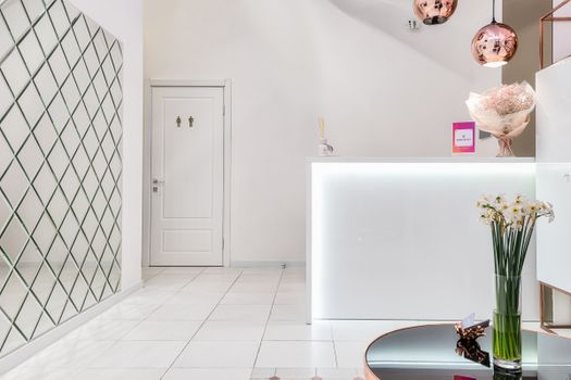Creative design of lobby with blooming flowers on table against counter with nameplate under decorative lamps