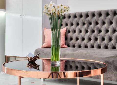 Blooming Narcissus bouquet in vase against couch in modern lobby