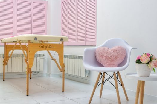Creative design of massage parlor with table and decorative heart shaped cushion in armchair on tiled floor