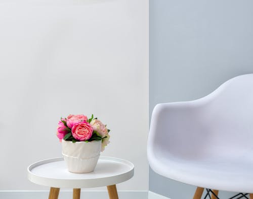 White armchair near round table with blooming peonies in ceramic pot in modern room