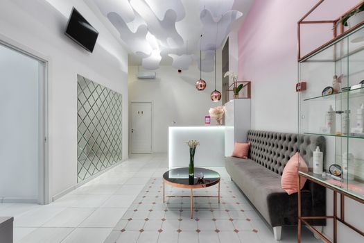 Interior of contemporary reception hall with sofa and glass table with TV set hanging on wall in beauty salon