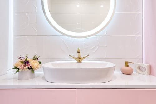 Free Interior of modern bathroom with luminous mirror hanging under sink with faucet near blooming flowers and soap Stock Photo
