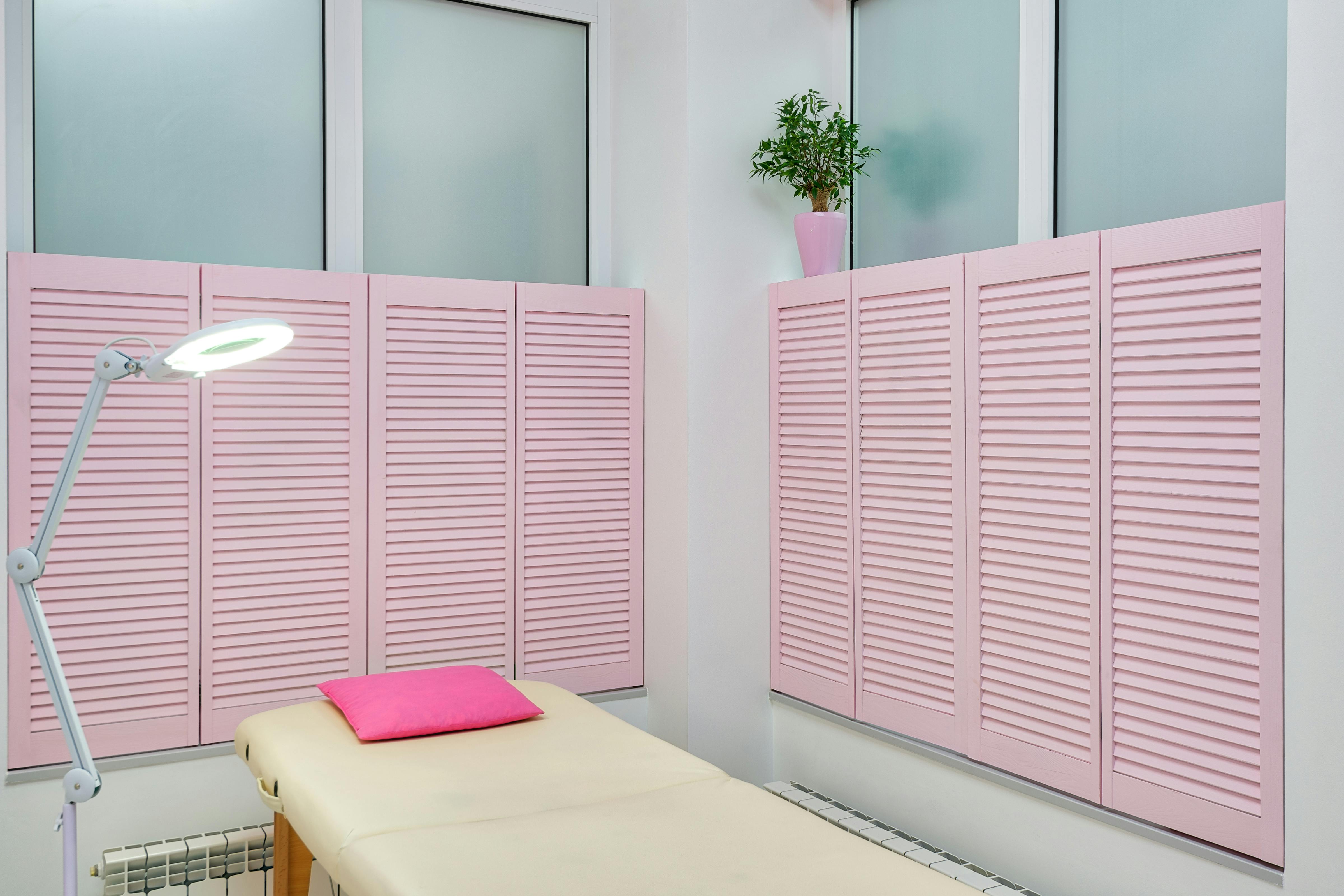 Interior of contemporary spa salon with couch under bright light of lamp with pink shutters on windows