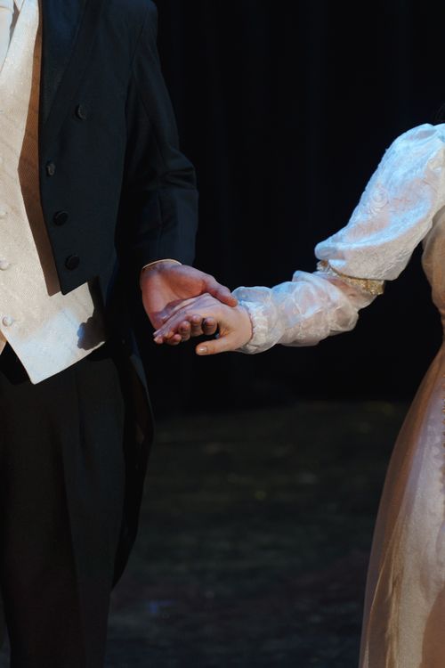 Free A close-up of two costumed performers holding hands on stage, evoking romance in a theatrical setting. Stock Photo