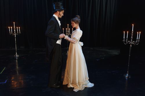 Free A romantic vintage theater scene with two actors in period costumes holding hands under candlelight. Stock Photo
