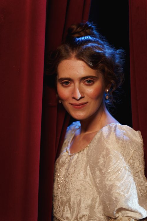 Free Portrait of a woman in vintage costume amidst theater curtains, exuding classical elegance. Stock Photo