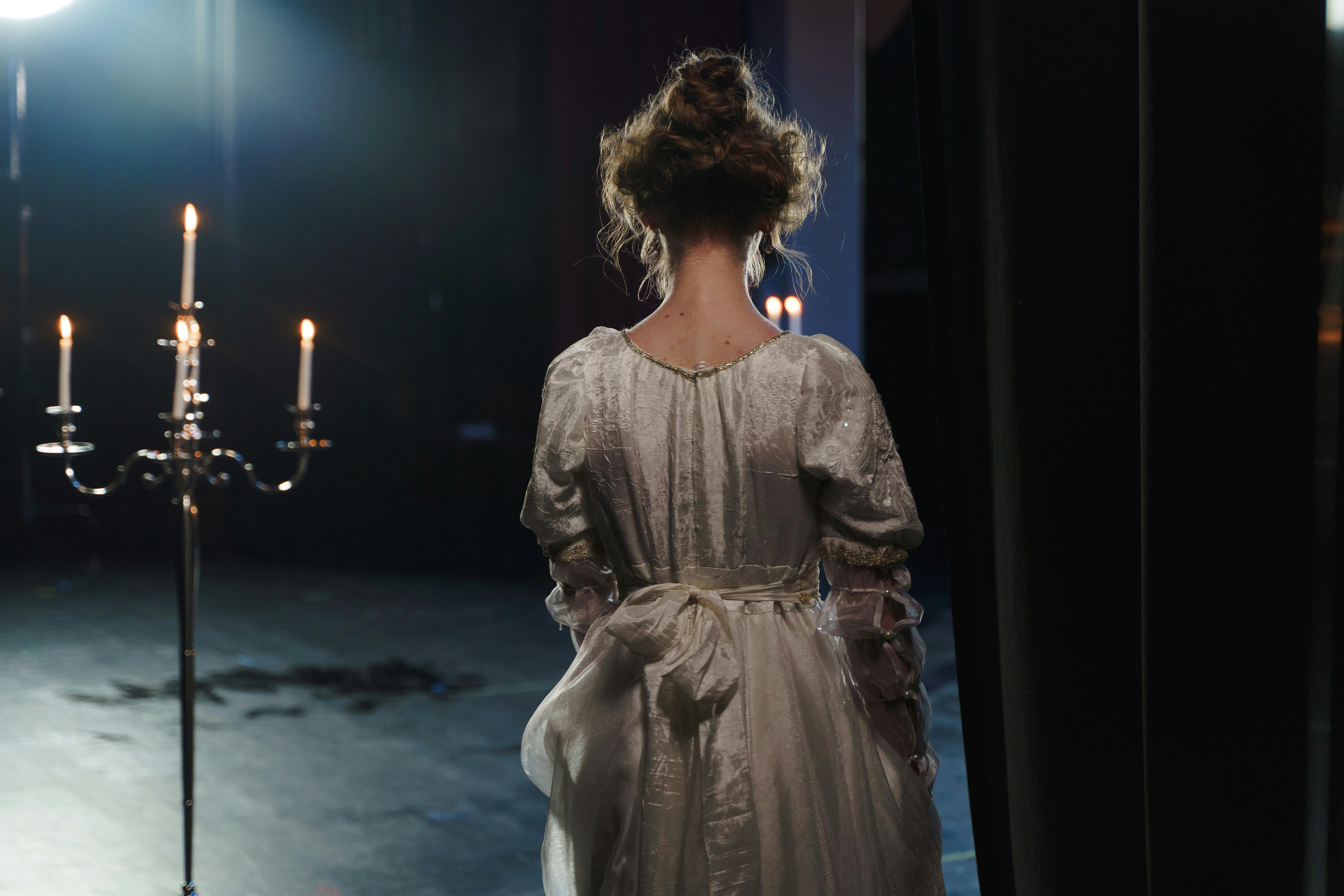 woman in white dress standing beside a curtain and candelabrum