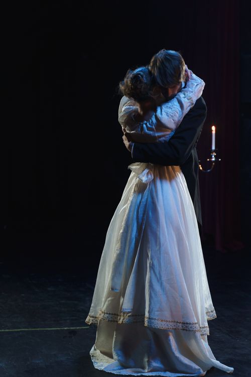 Free A couple embraces in a dramatic, dimly lit theater scene, evoking romance. Stock Photo