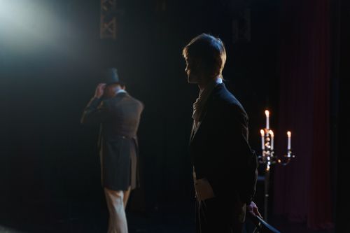 Free Two actors in Victorian costumes perform a dramatic scene on stage, lit by candlelight. Stock Photo