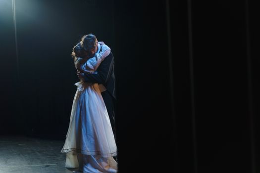 Couple embraces on stage, creating a dramatic and romantic moment in theatrical setting.