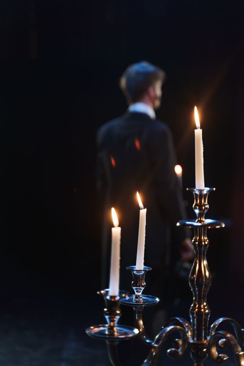 Free A theatrical scene with a man walking by candlelight on a dark stage, creating a dramatic mood. Stock Photo