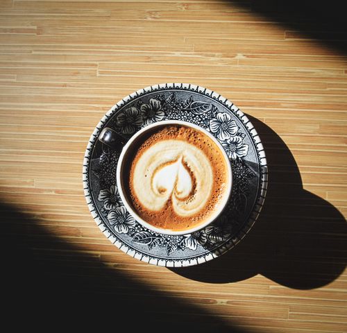 Free A beautifully crafted latte with heart design in a decorative cup on a wooden table. Stock Photo