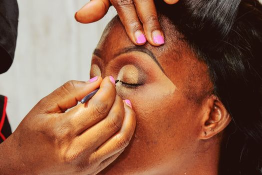 A close-up of a woman's face receiving professional makeup application, highlighting her eye makeup.