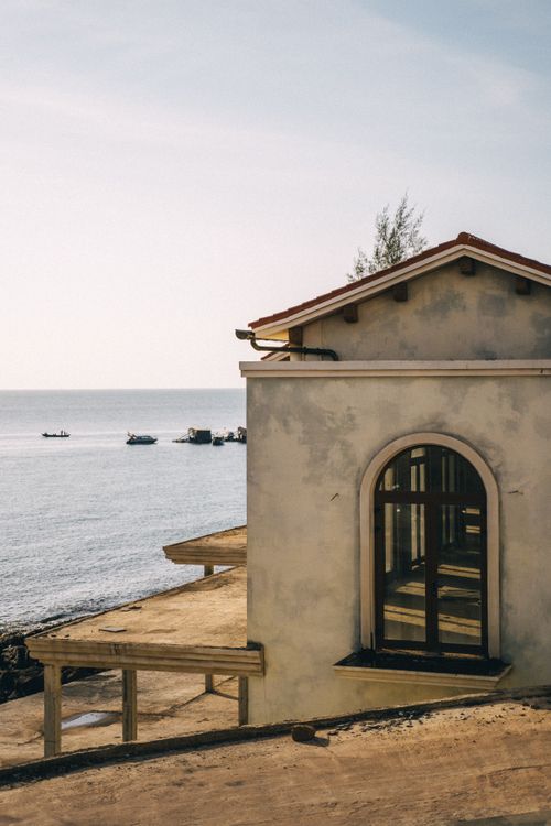Free A tranquil coastal house with an arched window facing the calm ocean. Perfect vacation spot. Stock Photo