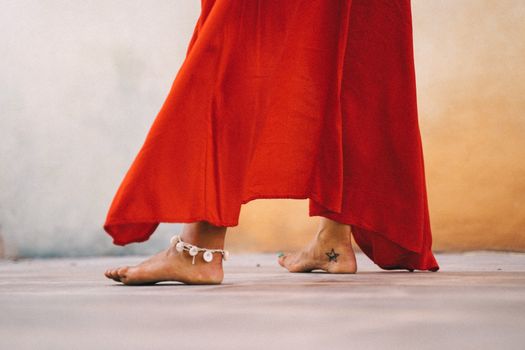 Close-up of a woman dancing barefoot in a flowing red dress with anklet outdoors.