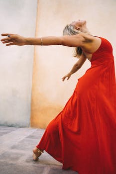 A woman in a vibrant red dress performs a graceful dance pose outdoors, embodying elegance and motion.