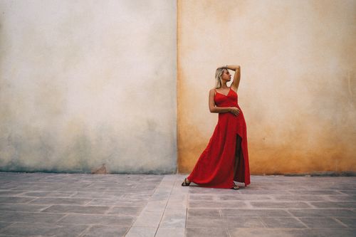 Free Stylish woman in vibrant red dress poses against a rustic wall, exuding confidence and grace. Stock Photo