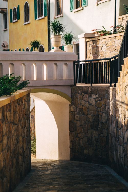 Free A picturesque Italian-style street with vibrant facades, archway, and lush greenery. Stock Photo
