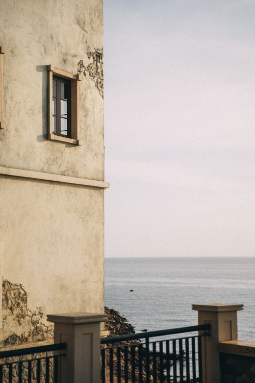 Free Side view of a vintage building exterior overlooking a serene ocean, offering a tranquil coastal scene. Stock Photo