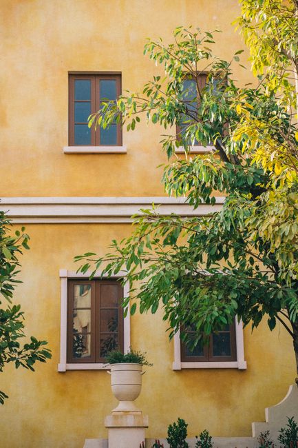Beautiful yellow building exterior with windows and lush green foliage.