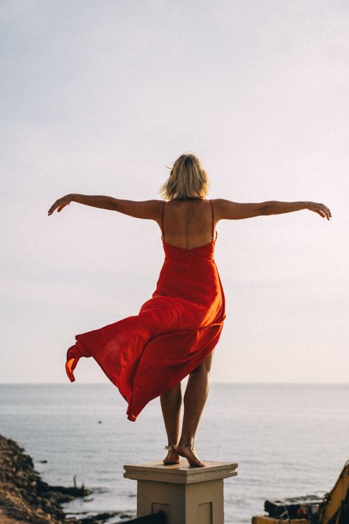 Free A woman in a flowing red dress stands with arms outstretched overlooking the sea, symbolizing freedom. Stock Photo