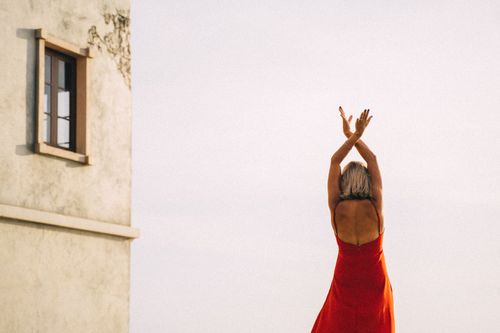 Free Woman in a red dress dancing outside by a building, expressing freedom and joy. Stock Photo