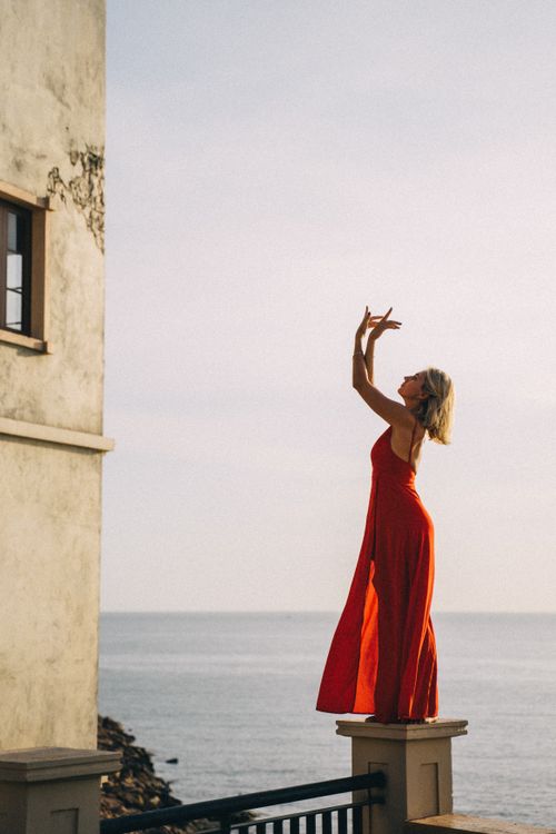 Free Graceful woman posing in a red dress by the seaside during sunset, combining elegance and nature. Stock Photo