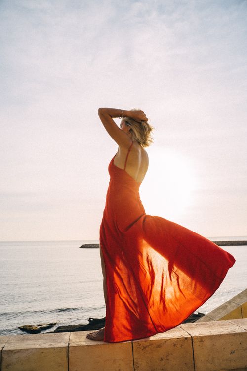 Free Woman in red dress gracefully standing by the ocean at sunset, capturing serenity. Stock Photo