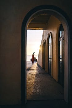 Silhouette of a dancer at sunset through an elegant archway on a beach.