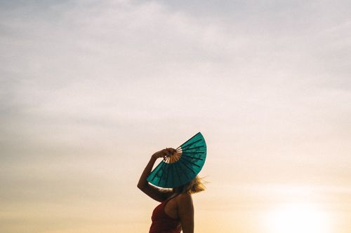Free A captivating silhouette of a woman with a hand fan against a warm sunset sky. Stock Photo