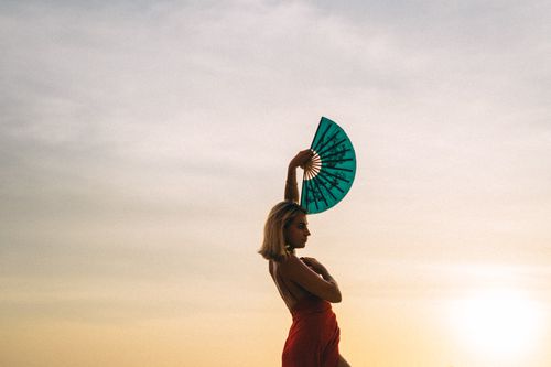 Free A graceful dancer silhouettes against a sunset holding a vibrant fan. Stock Photo