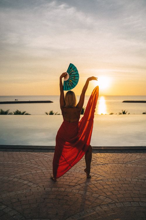 Free Silhouette of a woman with a fan dancing by the ocean at sunset, exuding grace and elegance. Stock Photo