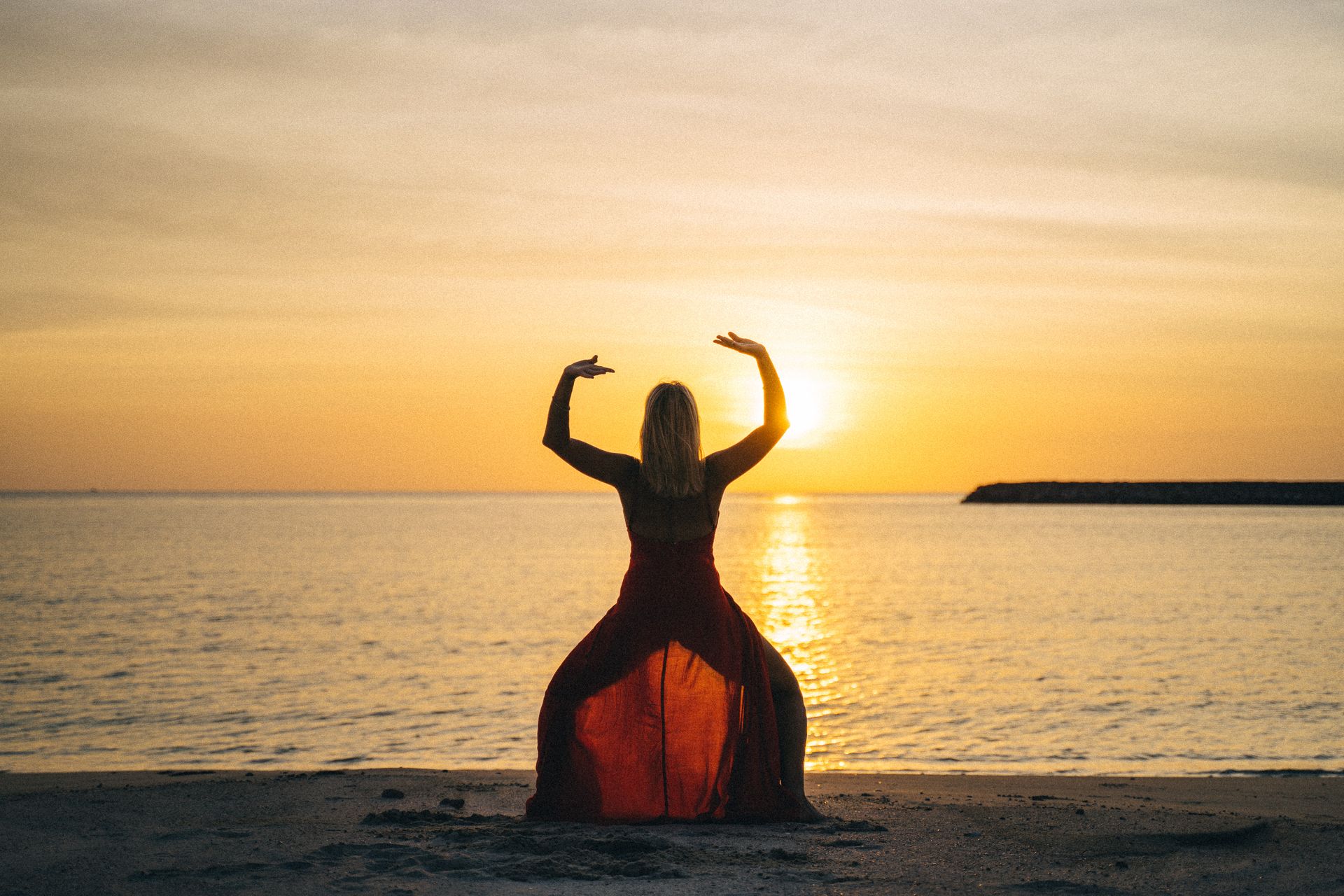Femme en posture face à la mer au coucher du soleil