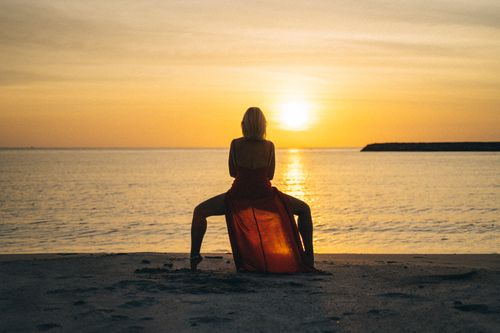 Free A woman in a red dress performs yoga at sunset on a serene beach. Stock Photo