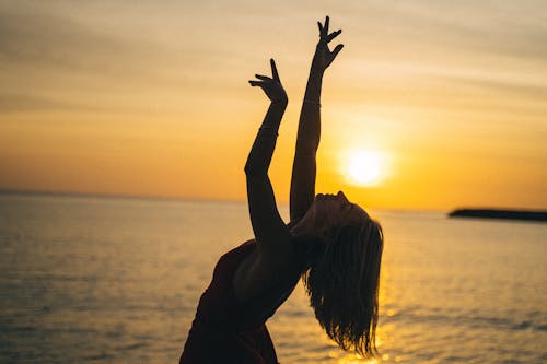 A Woman Raising Her Hands Beside the Beach