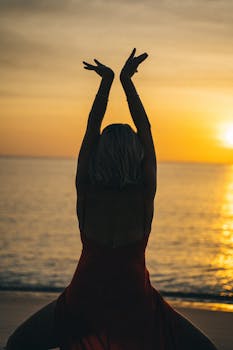 Silhouette of a woman dancing gracefully in a red dress on the beach during a stunning sunset.