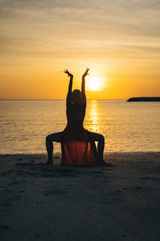 A woman in a red dress performing yoga on a beach during a breathtaking sunset.