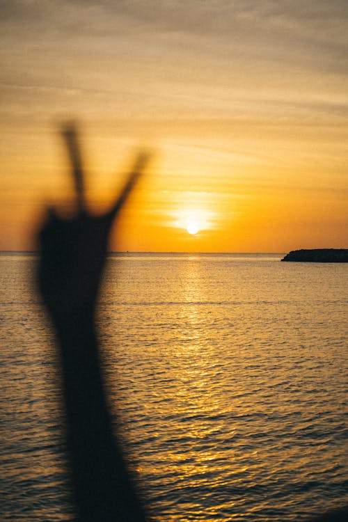 Arm Held in the Air Showing Peace Sign on the Background of the Sea at Sunset 