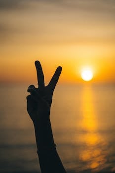 Silhouette of a hand showing peace sign against a vibrant sunset over the ocean in Vietnam.
