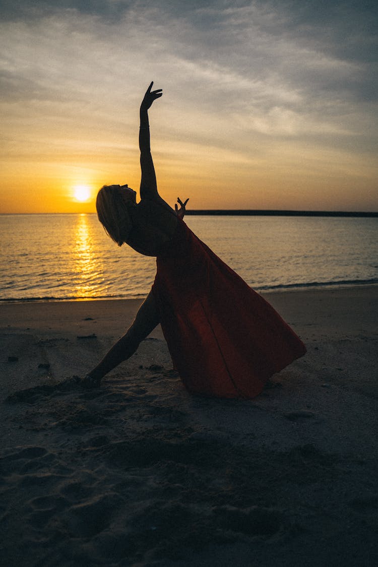 A Woman Dancing On The Shore While The Sun Sets