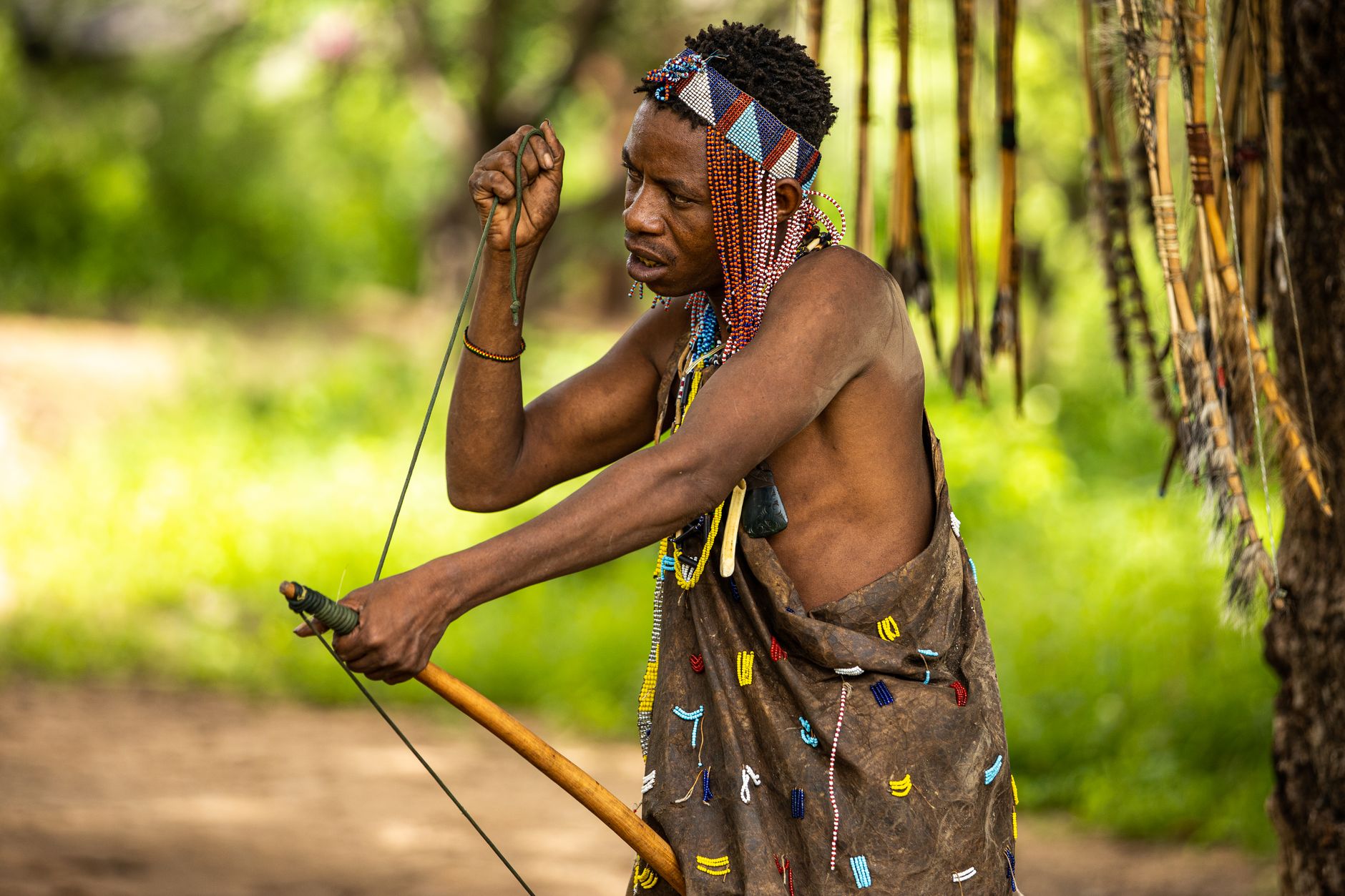 Portrait of a man in traditional tribal attire with a bow, outdoors in a lush setting.