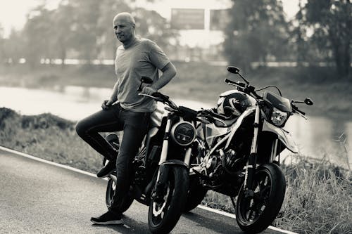 Free Grayscale Photo of a Man Standing Beside a Motorbike Stock Photo