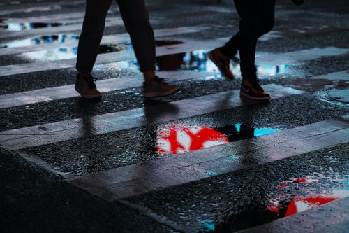 Free Two people walk across a wet crosswalk with vibrant reflections at night. Stock Photo