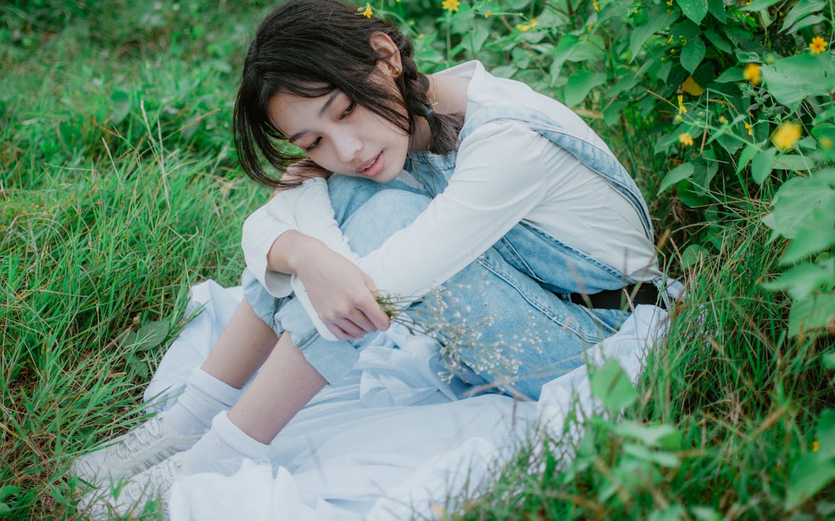 A Young Woman Sitting on Green Grass Holding Baby's Breath Flowers