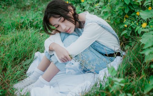Free A young woman sitting in a grassy field, surrounded by flowers, exuding calmness. Stock Photo