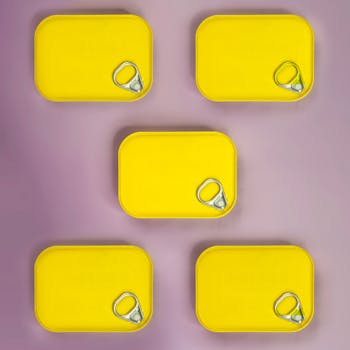 Creative display of closed yellow tins on a light purple background in a flat lay square format.