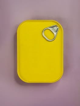 Yellow can with a pull tab placed on a pink background, viewed from above.